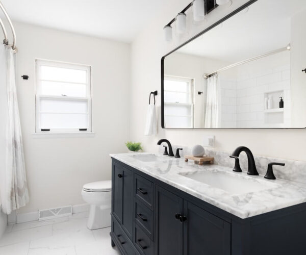 A beautiful bathroom with a dark blue sink, a marble countertop, and a large mirror under the light.