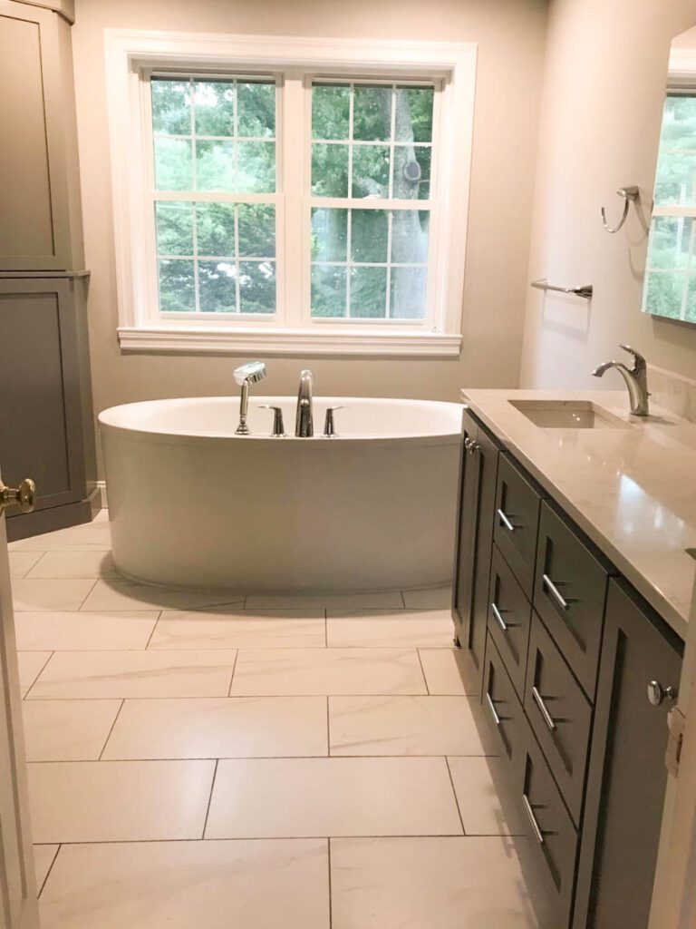 Soaking tub with window above it with a dark cabinet vanity