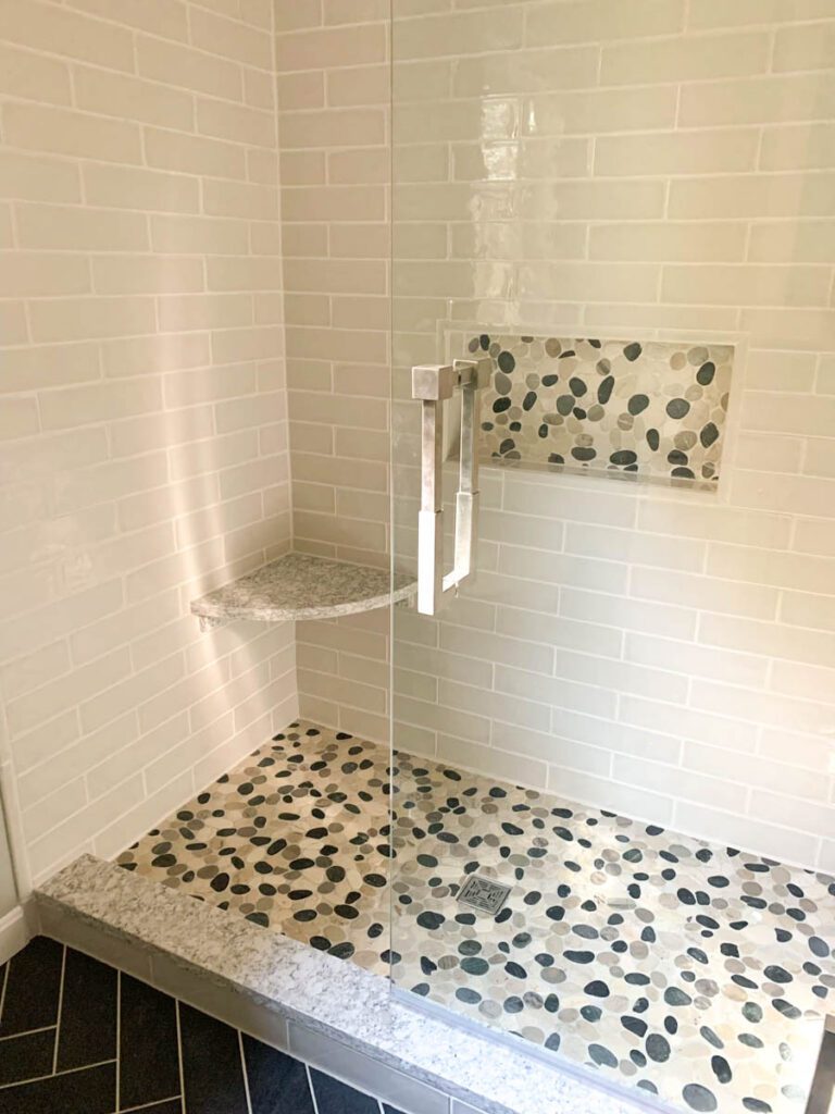 Tiled shower with a pebbled title floor and glass doors